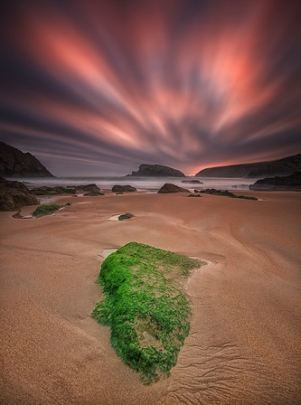A wild Cantabrian beach beneath a dramatic sunset sky near Liencres